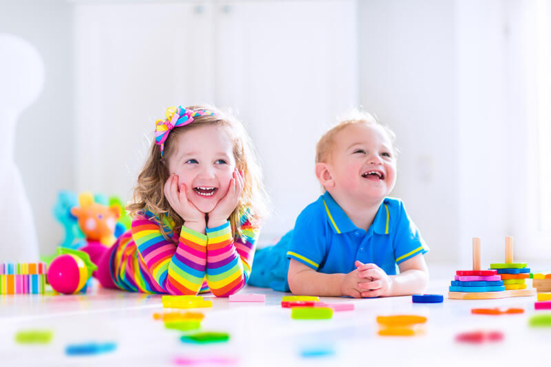 Two children are playing with colorful blocks on the floor.